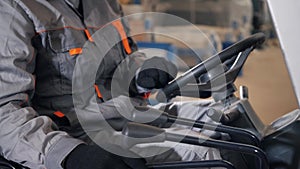 Close - up steering wheel and levers. man driving a forklift through a warehouse in a factory. driver in uniform and