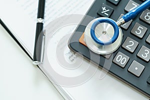 Close up of stethoscope on calculator and bill with pen