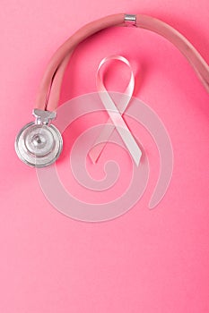 Close-up of stethoscope with pink breast cancer awareness ribbon on pink background, copy space