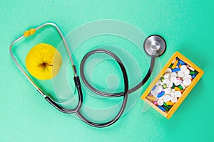 Close-up stethoscope and yellow apple on light green background with pills in wooden box. Top views