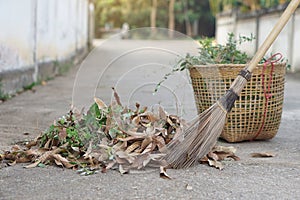 Close up stick broom sweeps dry leaves and weeds, keep into basket to for throw away garbage.