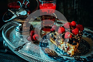 Close up still life in royal style. Close up piece of chocolate cake with raspberries on old blue plate, beside glass fruit drink