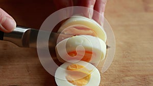 A close-up stock video capturing the hands of a woman delicately slicing a boiled egg on a wooden cutting board