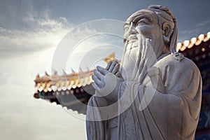 Close-up of stone statue of Confucius, pagoda roof in the background photo