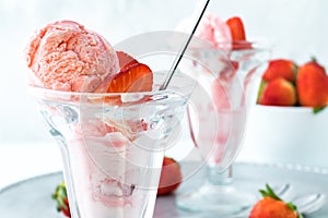 A close up of a strawberry ice cream sundae with another one in behind and a bowl of strawberries.