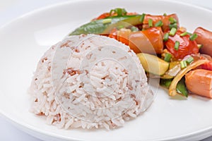 Close-up stream brown rice with blurred background of fried sausages and mixed vegetables in ketchup sauce, healthy eating