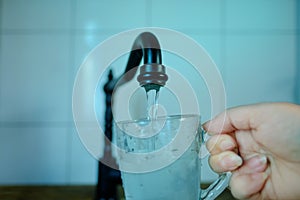 Close-up of stream of water flowing from a black water faucet in a kitchen in retro style, female hand picks up water in glass,