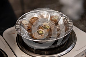 Close up street fast food take away portion of cooked escargot snails with French herbs. cooking on a miniature electric stove