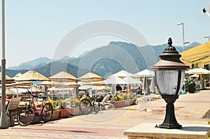 Close-up of a street lantern with bicycles, beach umbrellas and mountains on a backround