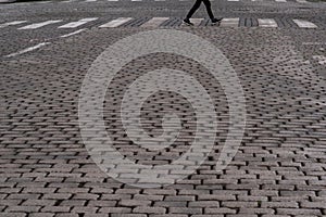 Close up of a street made of cobblestones, while someone is crossing the cross sign.