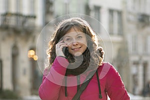 Close-up of a street portrait of a cheerful, successful middle-aged woman with delicate features talking on the phone.