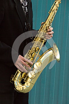 Close up of street saxophone Player hands playing alto sax musical instrument over blue background , closeup with copy