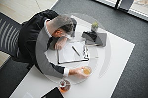 Close up of stressed businessman holding a glass of whiskey he sleeping and Data Charts,business document at office desk