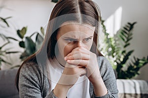 Close up of stressful sad young caucasian woman sitting alone on couch in living room covering face with hands. Emotional brunette