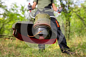 Close up of string grass cutting trimmer held by worker in protective clothing. Gardening concept