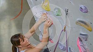 CLOSE UP: Strong woman reaches up to grip a crimp hold while lead climbing.