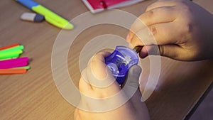 Close-up student hands sharpen a pencil in a blue sharpener.