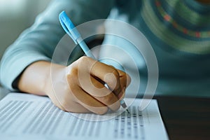 Close up of student`s hand holds a pen write on answer sheet. Student answers multiple choice questions on wooden table in examin