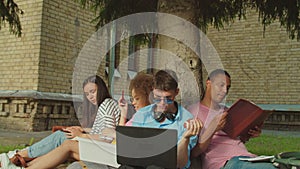 Close-up of students studying using gadget sitting under tree outdoors