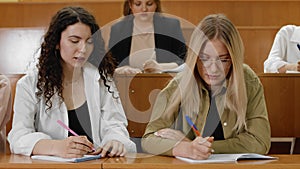 Close-up of students writing a lecture. The girl writes off the test work from a classmate. A group of students is