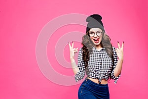 Close up studio portrait of cheerful blonde hipster girl going crazy making funny face and showing her tongue. Pink wall