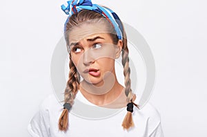 Close-up studio portrait of thoughtful blonde beautiful young woman wears wghite t-shirt, blue headband and braids hairstyle,