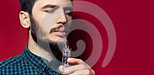 Close-up studio portrait of young man doing respiration treatment with classic inhalator and essential oil. Isolated on red backgr