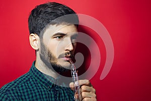 Close-up studio portrait of young man doing respiration treatment with classic inhalator and essential oil. Isolated on red backgr