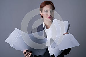 Close-up. Studio portrait of a young red-haired business woman, with red lipstick, and a gray business jacket, holding many blank