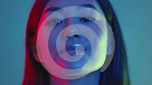 Close up studio portrait of young trendy happy asian lady posing and smiling to camera in red and blue neon lights