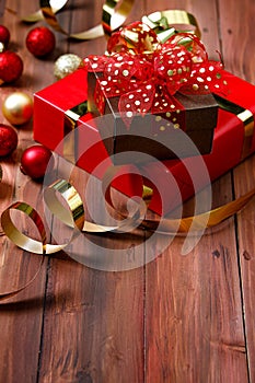 Close up studio shot of small brown present gift with gold dot on red ribbon bow tie placed on big paper wrapped box on dark brown