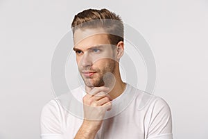 Close-up studio shot thoughtful, focused blond handsome man, touching chin, look away concentrated, having idea