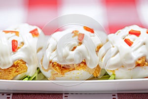 Close up of Stuffed eggs with tuna, tomato, mayonnaise and red pepper on red tablecloth.