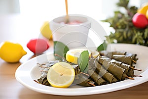 close-up of stuffed vine leaves on white plate, lemon slices on side