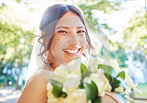 Close up of a stunning bride smiling while holding a bouquet of white roses and standing outside on a sunny day. A happy