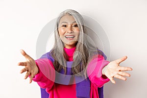 Close-up of stylish asian mature woman reaching hands forward, stretching arms for hug or hold something, smiling happy