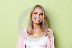 Close-up of stylish blond girl smiling, looking confident, standing over green background