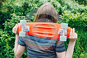 close up stylish girl carrying the penny board on the background of green trees