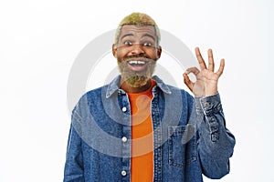 Close up of stylish hipster guy shows okay sign. Handsome african american man with yellow beard and hairstyle, makes ok