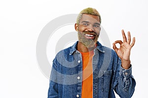 Close up of stylish hipster guy shows okay sign. Handsome african american man with yellow beard and hairstyle, makes ok