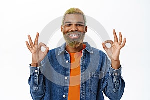 Close up of stylish hipster guy shows okay sign. Handsome african american man with yellow beard and hairstyle, makes ok