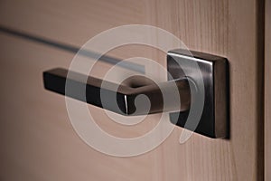 Close up of stylish silver chrome door handle on modern interior door. Stylish light brown door with frosted glass