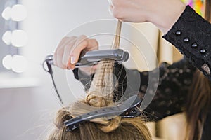 Close up of stylist hands with styling iron straightening woman hair