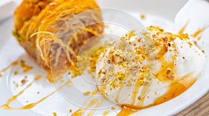 Close up of a succulent Greek dessert. Greek kataifi with honey yogurt and grated pistachios on a white plate and a blurred