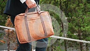 Close up of suitcase was held by profession businessman at green city. Urbane.