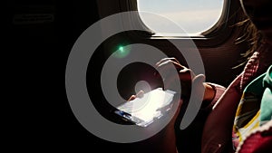Close-up. the sun`s rays are reflected in the phone. dark silhouette of kid hands and mobile phone against airplane`s