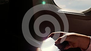 Close-up. the sun`s rays are reflected in the phone. dark silhouette of kid hands and mobile phone against airplane`s