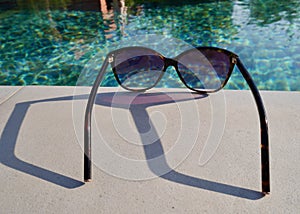 Close up of sunglasses at swimming pool. Summertime background, holidays, travel concept.