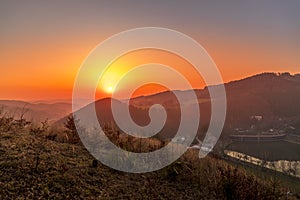 Close up sunset timelapse when sun is behind hills and mountains full of trees and moving clouds behind which sun sets a strong