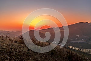 Close up sunset timelapse when sun is behind hills and mountains full of trees and moving clouds behind which sun sets a strong